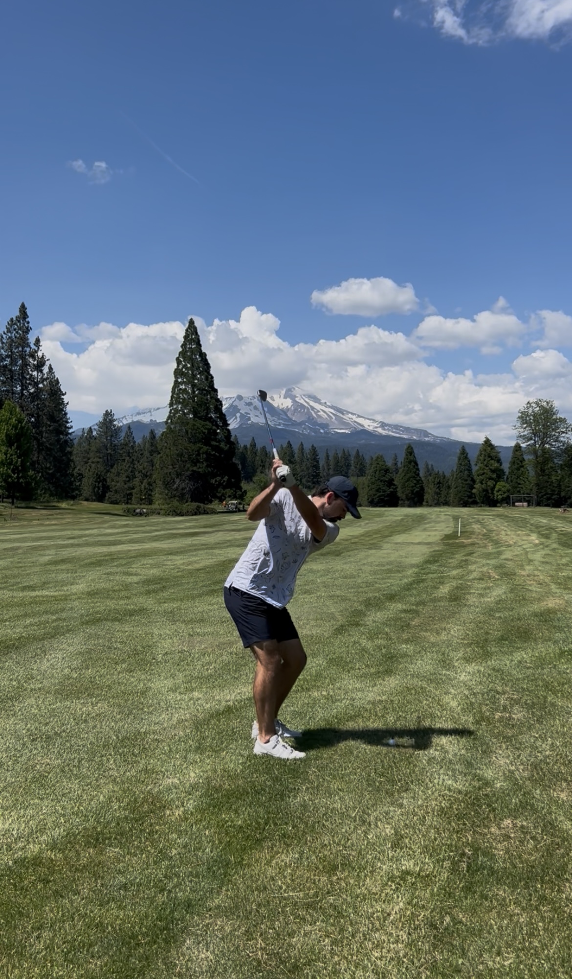 Golfer mid-swing on a golf course with Mount Shasta in the background